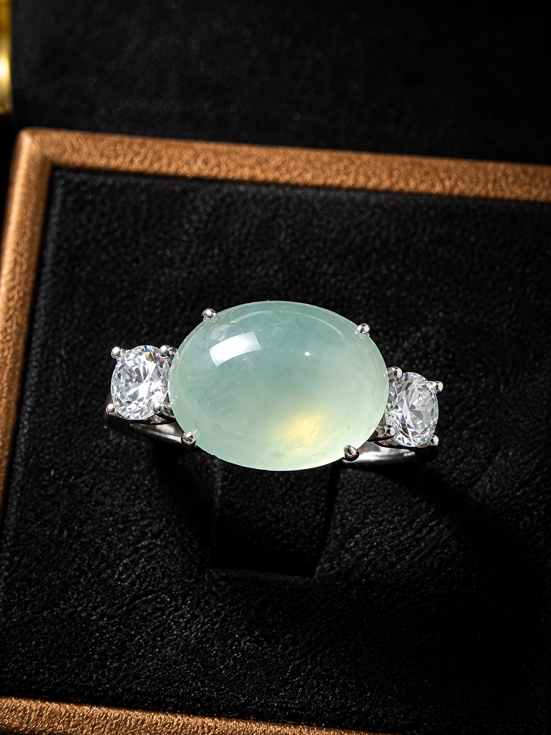 Nhẫn phỉ thúy Jadeite cabochon oval xanh băng thiên nhiên đính hai viên đá trắng đối xứng sang trọng.
